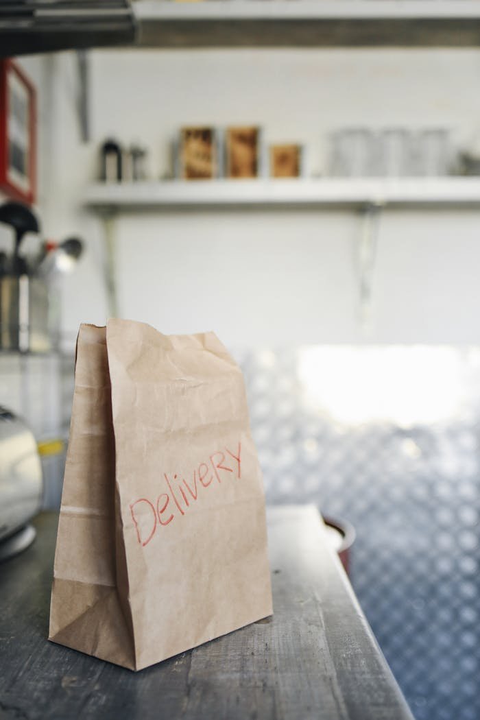 portfolio-01 Brown paper delivery bag resting on a wooden table in a bright indoor setting.