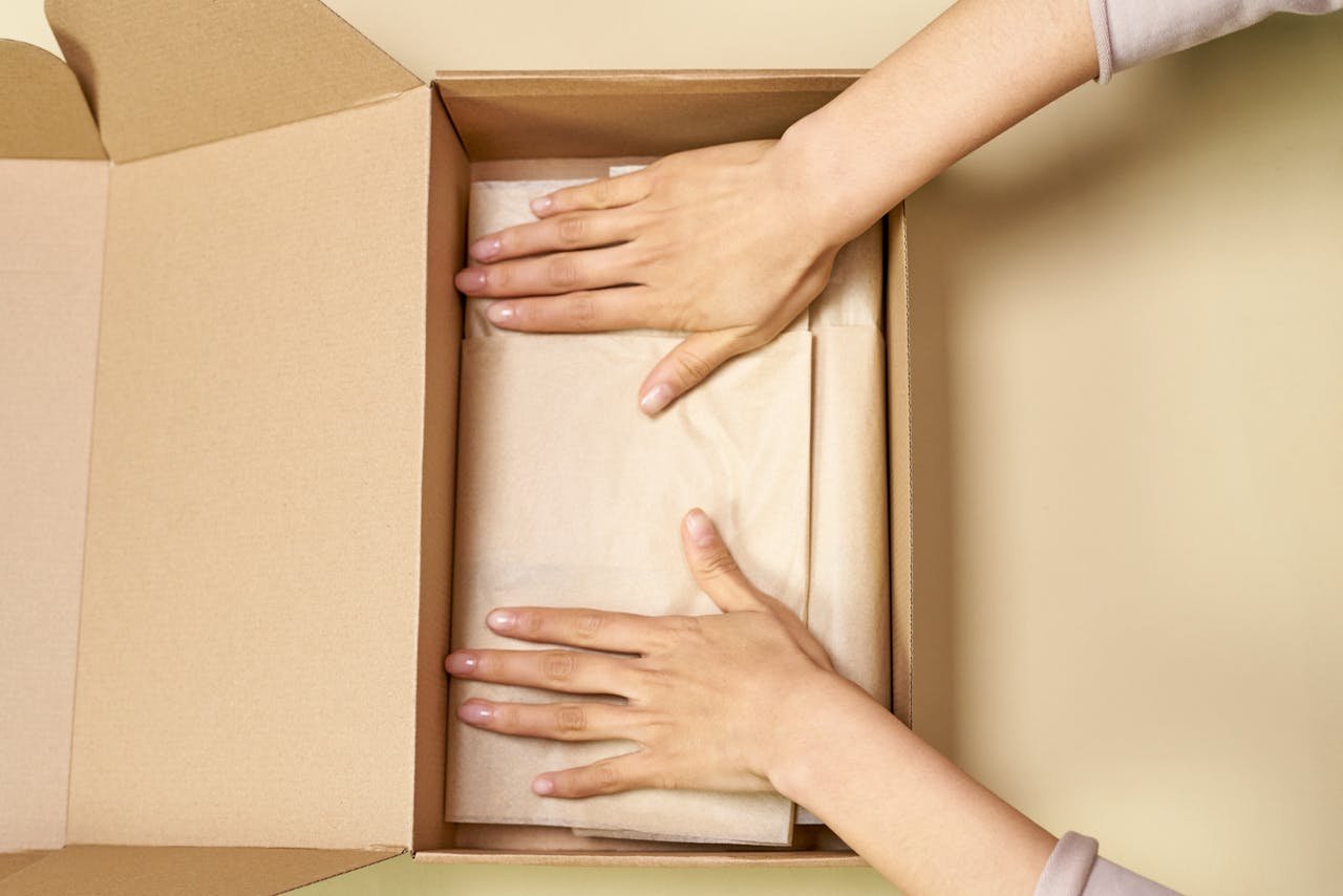 portfolio-05 Close-up of hands packing a cardboard box with care using parchment paper.